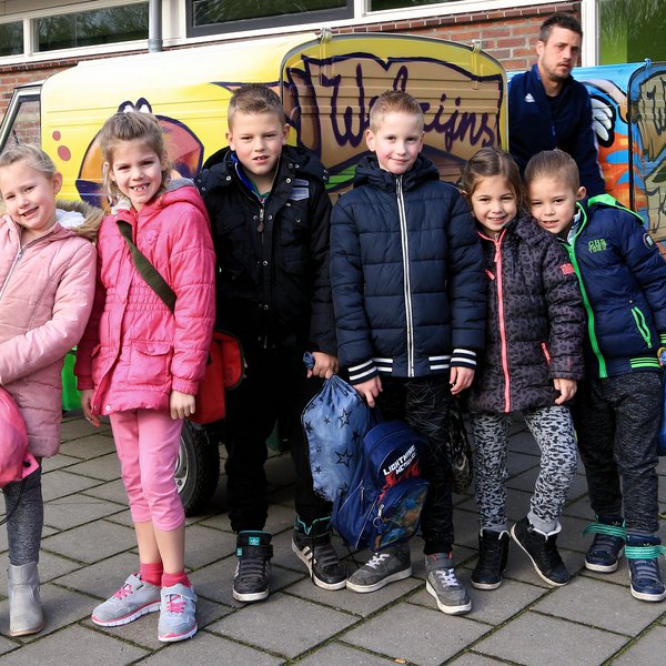 zes kinderen met hun schooltassen die voor de welzijnskwartier bussen staan