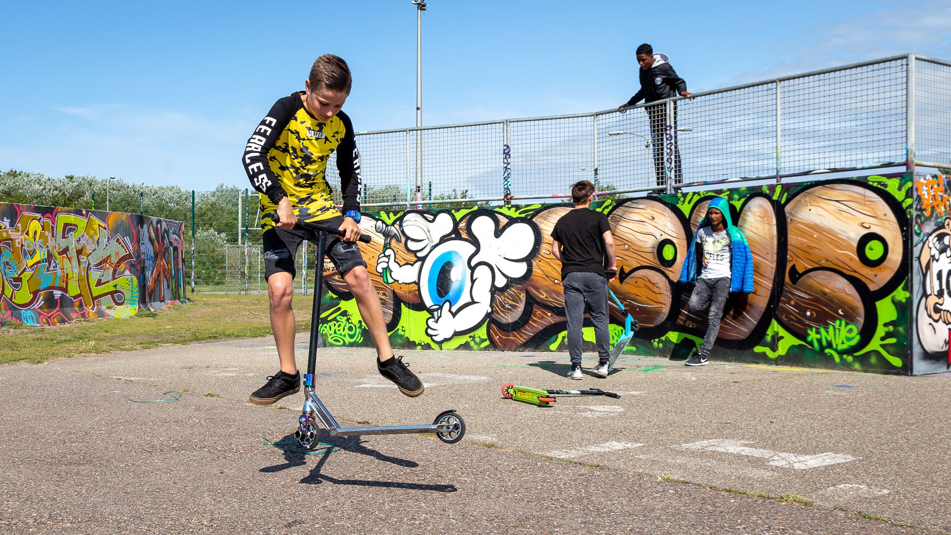 jongeren op skatebaan spelen met step en skateboard