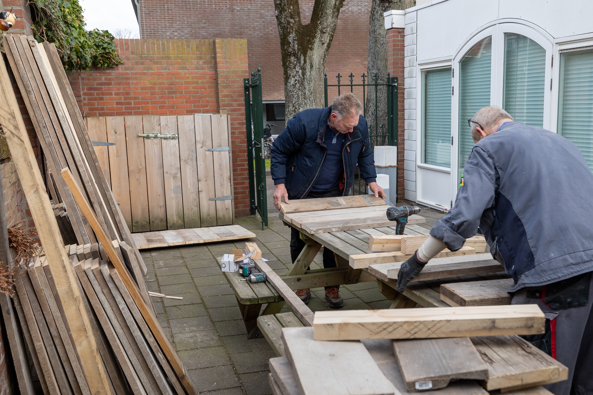 Twee mannen zijn buiten bezig met het afmeten van houten palen en planken